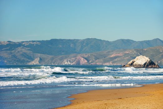 Ocean Beach in San Francisco California with waves coming to the sand and Marin County and blue sky background.