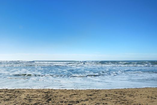 Ocean Beach in San Francisco California with waves coming to the sand and blue sky background.