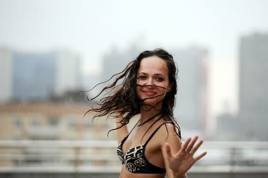 The beautiful woman dances on a roof under a rain