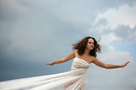 The girl in a white fabric on a background of the sky
