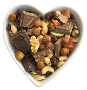 Heart shaped bowl filled with dried fruits, nuts, dark chocolate and milk chocolate.