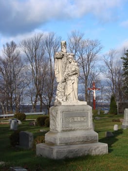 White marble statue of Mary in Catholic Cemetery. Statue has moss and lichen on it. Fall day with bright blue sky and clouds.