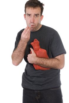 A young man taking his temperature with a digital thermometer and holding a hot water bottle to his side, isolated against a white background