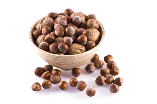Hazelnuts and walnuts in and around a wooden bowl, isolated on white. 