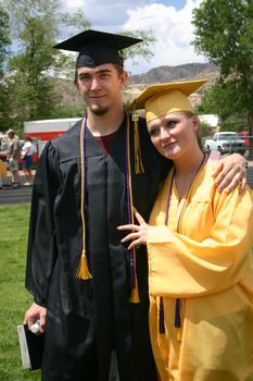 Two graduating students in their caps and gowns and gold honor cords