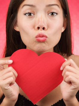 Valentines day kiss? Woman blowing a kiss holding a Valentines Day heart sign. Beautiful mixed race chinese / caucasian model.