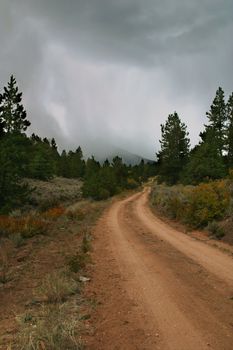 High mountain ATV trail leading up an autumn landscape into an approaching thunderstorm with rain, mists, and potential snow.