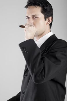 A good looking young business man somking a cigar, in a studio shot.