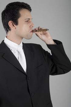 A good looking young business man somking a cigar, in a studio shot.