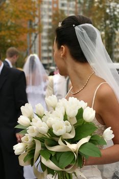 The bride with a bouquet from white tulips looks following to a newly-married couple