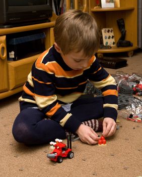 The boy sits on the floor and plays in the constructor.