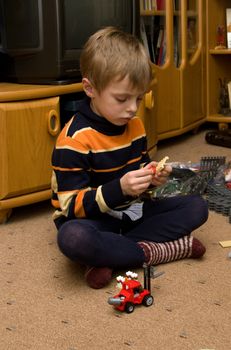 The boy sits on the floor and plays in the meccano.