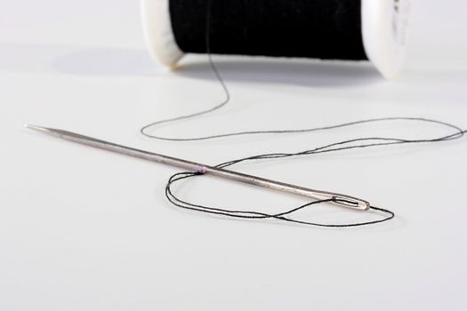 Needle with a black thread which is connected to the coil on a background.