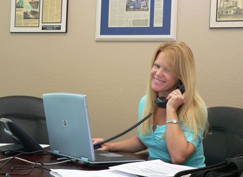 Pretty blond woman busy at office desk and on phone