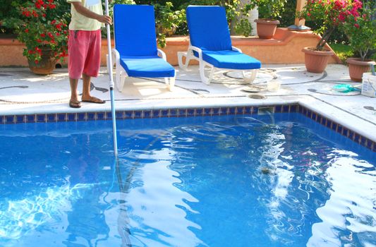 man cleaning pool with large pole and lots of flowers