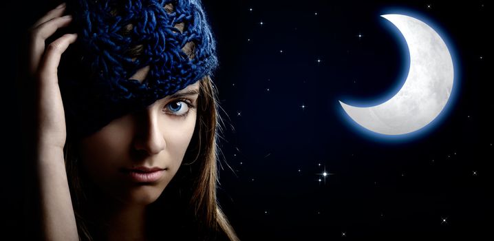 Portrait of a beautiful and young woman at night with a artifical moon on the background