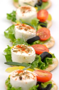 Small goat cheese slices on cracker with salad leaf, tomato, olive and spices