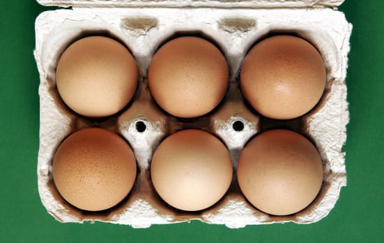 Six Brown Eggs In A Grey Cardboard Box On Green Background