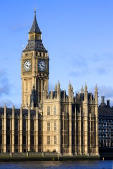 An evening shot of the Palace of Westminster, Big Ben and the River Thames, London England against a blue sky