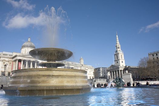 Close up of a fountain in Trafalgar Square with the National Gallery and St Martins in the Field in the background.