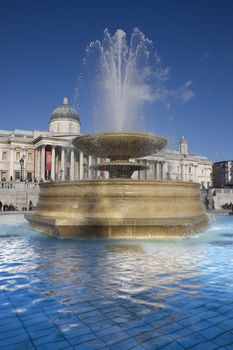 Close up of a fountain in Trafalgar Square with the National Gallery in the background.