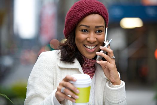 A modern business woman in the city talks on her cell phone while enjoying a cup of coffee.