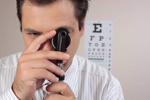 An optometrist turning the lens dial of the opthalmoscope while examining a patient's eyes.