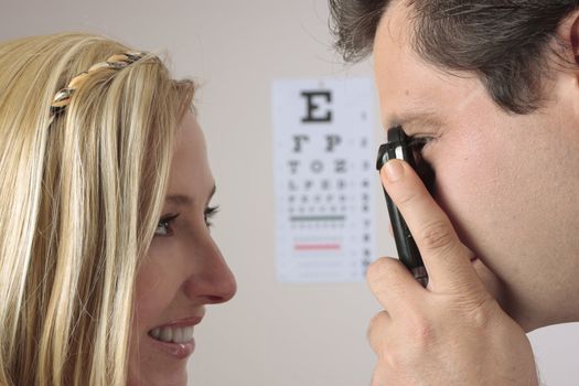 Closeup of a an optometrist eye doctor checking a female patient eyes.  Focus to man.