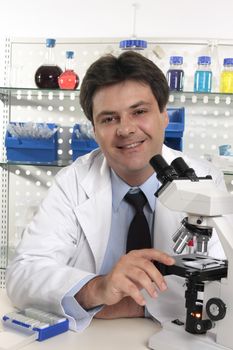 Smiling Scientific researcher sitting at laboratory desk  using a microscope for further analaysis of substances...