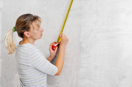 one young blonde with measure in hands at wall
