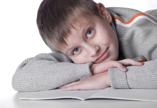 Young boy lying down on a floor with copy-book isolated on white