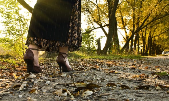 Young woman walking at autumnal park on yellow leaves