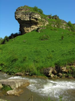 The rock covered with a grass above the river in the Caucasian mountains          