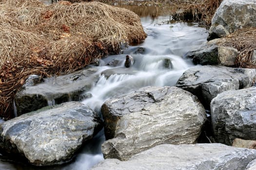 Small creek with rocks,stones and hay during winter - water blurred motion effect.