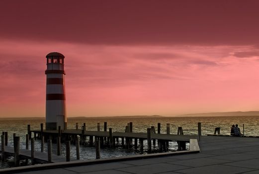 Two people sitting at a lighthouse enjoying the sunset.