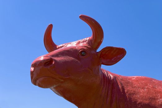 Portrait of  red plastic cow against a blue sky