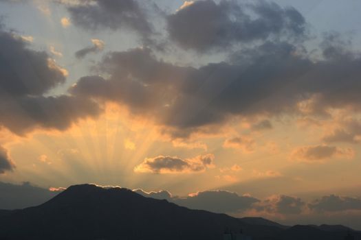 Dramatic Sunset in a beautiful landscape-mountain and sunbeams rays accentuating through thick clouds.