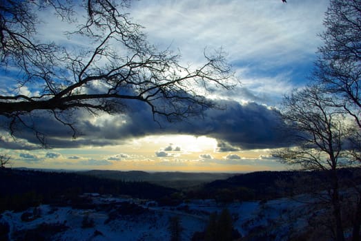 Bare branches and a dark landscape silhouetted against a post storm sunset