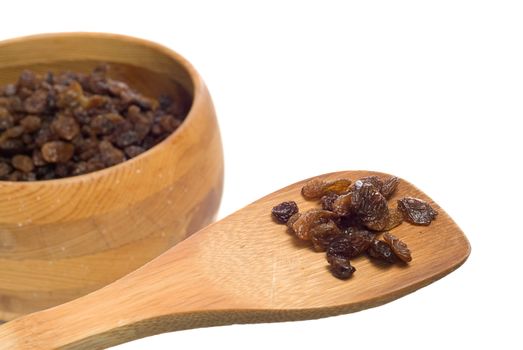 A small cluster of sundried raisins being displayed on a wooden spatula with more in a bowl OOF in the background