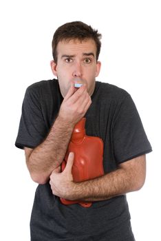A young man feeling ill can't make up his mind whether he feels hot or cold and is using a hot water bottle but wearing a short sleeve shirt, isolated on white