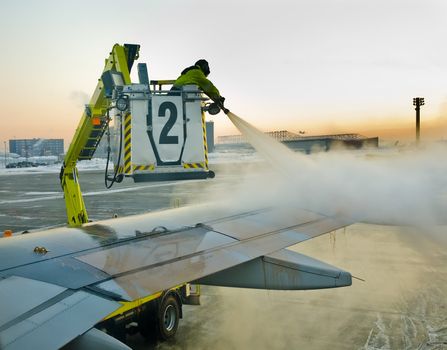 Man defrosting plane's wing before departure early in the morning