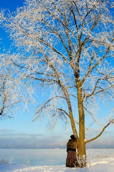 Woman stands near a tree on the bank of a frozen sea