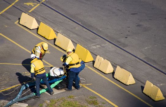 Four helmet longshoremen carry heave cable to moor the ship in port.