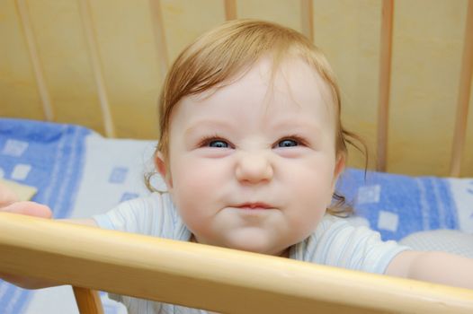 Funny grimace on baby boy face sitting in bed