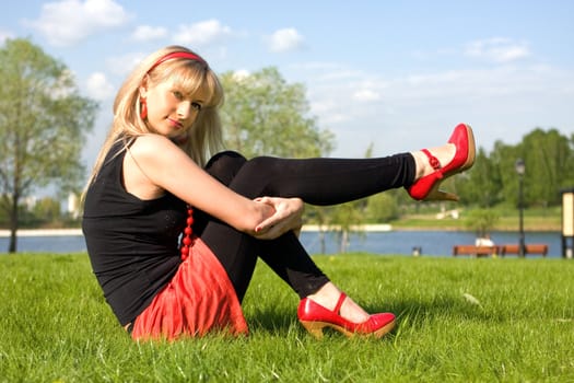 The girl sits on a grass on the bank of the river