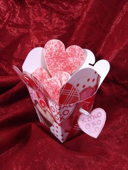 Heart shaped sugar cookies with red sugar in chinese take out carton decorated with hearts.Red background fabric.