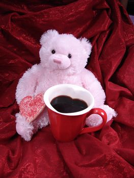 Pink Valentine bear with heart shaped cookie and heart coffee mug. Red fabric background.