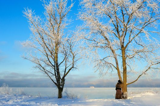 Woman stands near a tree on the icy shore