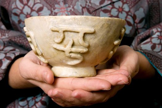 A woman's hands holding a natural jade bowl with four chinese heiroglyphs carved into the bowl.  The four chinese characters translated say "Four Seasons Always Coming Money" a good luck message.