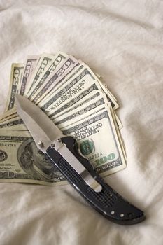 A knife and some fanned out cash laying on a bed.